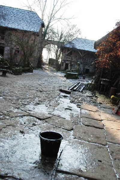 Winter auf der Mühle - ein Eimer steht auf einer zugefrorenen Pfütze. Der Innenhof der Mühle ist vereist.